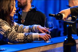 Woman in a black and white cable knit sweater holding a glass that wine is being poured into